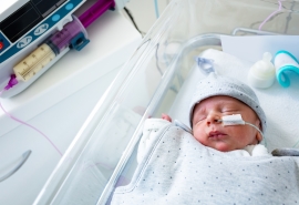 Bebé internado en un moisés al lado de la máquina en una sala de hospital.