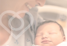 Madre sostiene un bebé recién nacido y lo mira sonriendo.