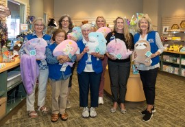 Cuatro voluntarios y tres enfermeras sostienen coloridos animales de peluche en la tienda de regalos de Skagit Valley Hospital.