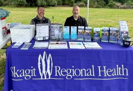 Paul Ross y Brian Schuman en la mesa de Skagit Regional Health durante un evento al aire libre.