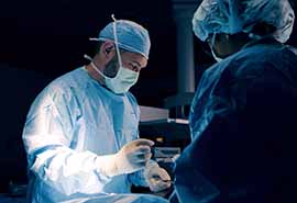 Cirujano con bata azul realizando una operación con un asistente